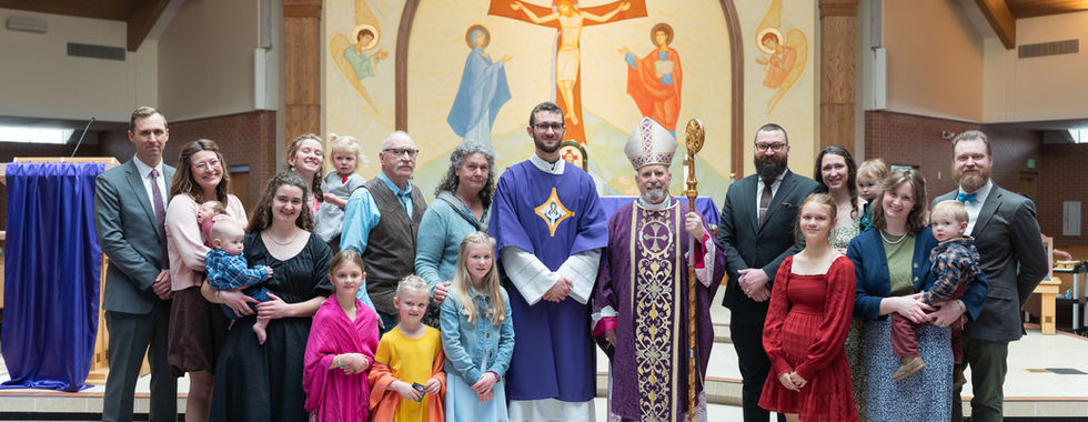 Group of people, including clergy in purple robes, posing in a church with a large religious mural. Children in colorful outfits.