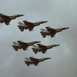 Six jet planes in formation fly against a cloudy sky, showcasing sleek designs with red and white patterns, evoking a sense of precision.