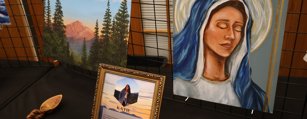 Religious paintings and framed tribute displays featured at a Catholic gala, including artwork of the Virgin Mary and a mountain landscape.