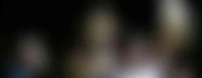 Priests holding a gold monstrance and candles process in a dimly lit setting. The atmosphere is solemn and reverent.