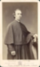 Sepia portrait of a Catholic priest in a dark robe standing beside a chair, with handwritten studio text and Denver, Colorado below.