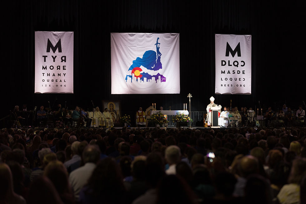 Grupo religioso en un escenario en un evento, con pancartas blancas y un fondo colorido detrás. Público numeroso observa. Ambiente solemne.