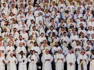 Sacerdotes en ropas blancas realizan un gesto de oración en grupo, mostrando concentración y solemnidad. Fondo oscuro y uniforme.