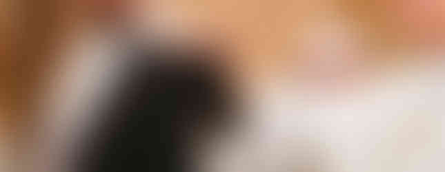 Priest in white robe touches a nun's black veil during a ceremony, with another person in the background. Warm, solemn atmosphere.