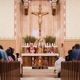 Catholic mass in a church: priests at the altar beneath a crucifix, with congregation kneeling in the pews.