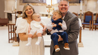 Smiling parents hold two dressed-up children in a church before the altar, creating a joyful family portrait.