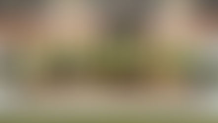 People in hard hats and yellow vests participate in a groundbreaking ceremony, holding shovels over soil, with a truck and building in the background.