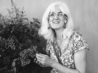 Smiling older woman with white hair and glasses holding flowers beside a leafy plant; banner reads Appeal in Action