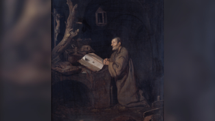 A monk kneels, praying at a desk with an open book in a dark, rustic room. A tree branch and animal skull create a somber mood.