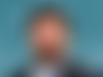 Smiling man with a beard in a blue suit and tie against a mottled teal background. The mood is positive and professional.