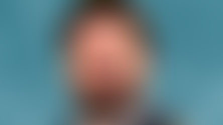 Smiling man with a beard in a blue suit and tie against a mottled teal background. The mood is positive and professional.