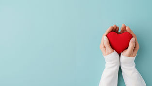 Hands in white sleeves hold a red heart against a pale blue background, conveying warmth and care.