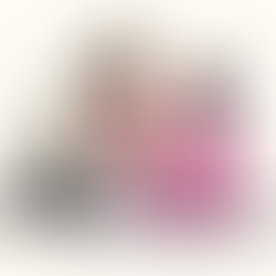 A bearded man in white, a woman in pink, and a baby in a purple wrap share an emotional moment on the ground, conveying tenderness.