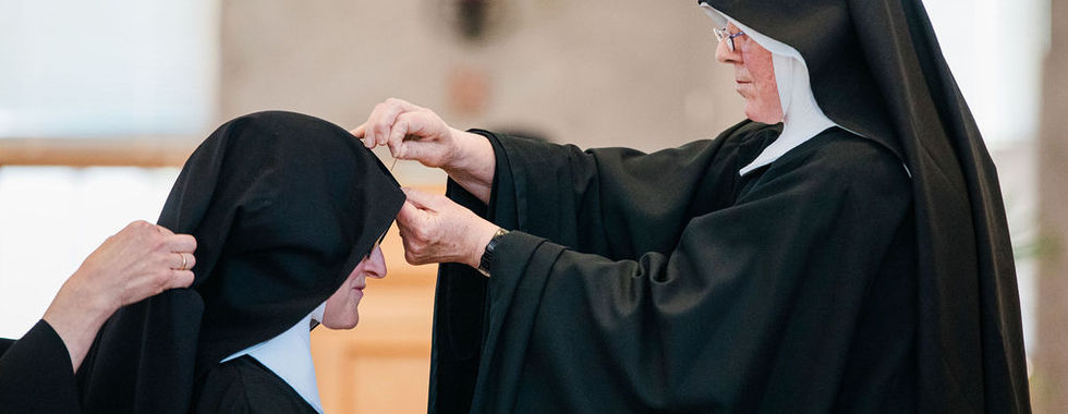A superior adjusts the veil of a religious sister during the rite of profession.