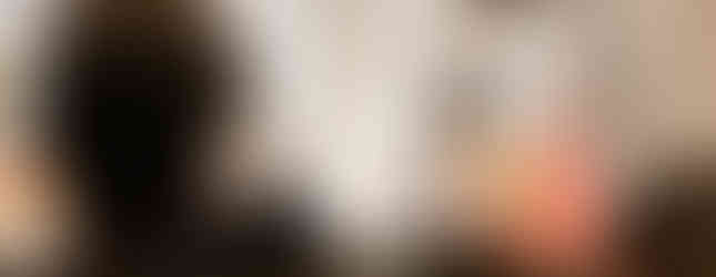 A woman speaks at a pulpit inside a grand church with ornate pillars. People sit in pews, listening. A crucifix and decorative red and gold element are visible.