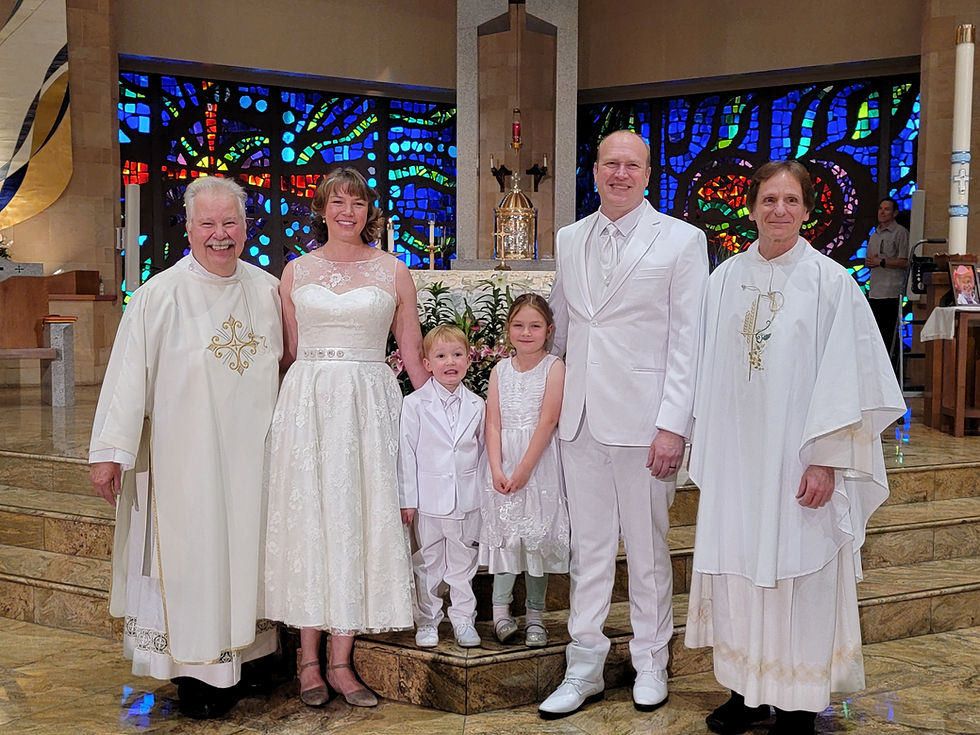 A family and two clergy in white attire smile inside a church with colorful stained-glass windows. The mood is joyful and celebratory.