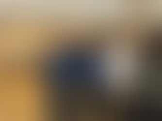 Three smiling men in casual clothes pose in a hall with wooden floors. Tables in the background have food trays. Warm lighting and a relaxed mood.