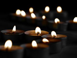Multiple lit tealight candles in black holders on a dark surface, creating a warm, serene glow against a black background.