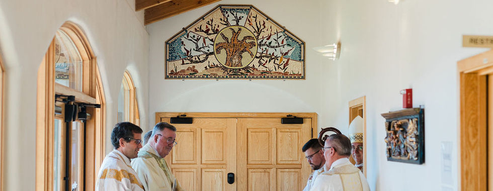 Priests and clergy members gather in a sunlit hallway before the start of a religious vows ceremony.
