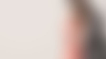 Couple embraces warmly, both in casual attire; the woman in pink, man in grey. Light background, soft and intimate mood.