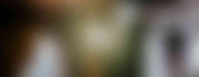 Person holding a golden ceremonial object in a dimly lit setting. Light glows from the object, casting a solemn mood in the background.