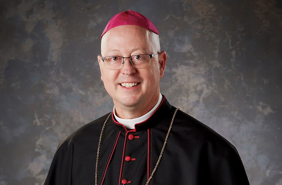 Smiling man in clerical dress with a magenta zucchetto and gold chain against a textured gray background.