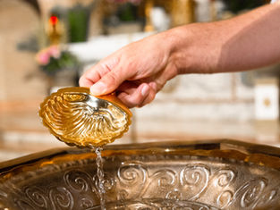 Mano sostiene una copa dorada en forma de concha y vierte líquido en un cuenco ornamentado; fondo desenfocado.