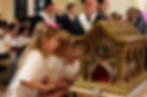 Three young girls in white shirts gaze at an ornate gold reliquary during a solemn church ceremony, with clergy blurred behind them.
