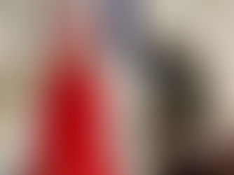 Bishop in red robe and pink zucchetto prays at a lectern in a church. Background features ornate altar, stained glass, and clergy.