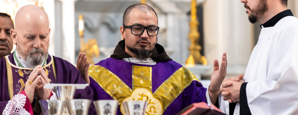Three clergy in a church, wearing purple and white robes, conduct a ceremony with silver chalices. The setting is ornate and solemn.