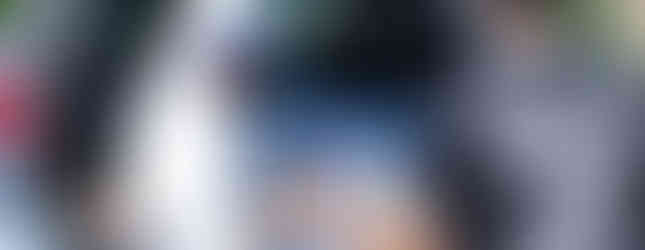 A woman in a headscarf serves food from a car trunk to a man in a "FAST JOE" shirt. Outdoor setting, bright day, giving mood.