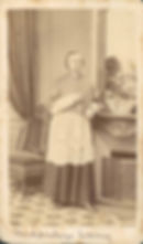 Sepia studio portrait of Archbishop Denny in clerical robes, standing by a fireplace and chair; handwritten caption below.