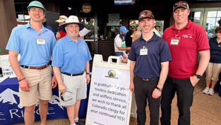 Four smiling men in golf attire pose outside a booth with a Catholic Radio Network thank-you sign at a scouting event.