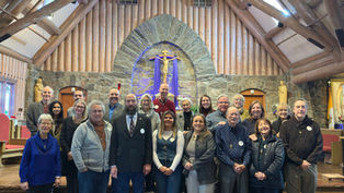 Group of people smiling in a church with wooden beams and stone walls. A crucifix is in the background, creating a warm and inviting atmosphere.
