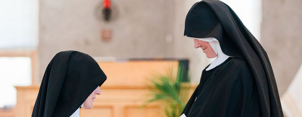 A religious sister kneels before her superior as vows are formally received during the ceremony.