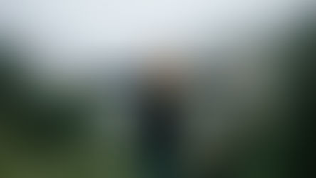 Woman in a dark coat stands with arms outstretched in a foggy, lush green mountain setting, expressing joy and freedom.