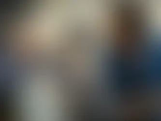 Elderly woman in wheelchair smiles at woman in blue cardigan touching her hand. They're in a hallway, conveying warmth and connection.