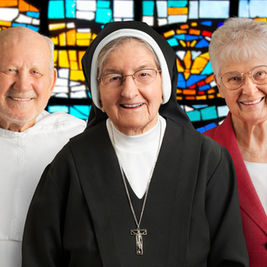 Three elderly people smiling, a priest, a nun, and a woman in a pink blazer. Colorful stained glass background enhances warmth.
