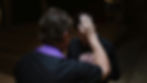 A priest in a purple stole raises his hand in blessing over a man with clasped hands in a dimly lit church.