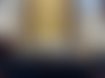 Church altar with a white cloth, crucifix on brick wall, and various urns and boxes on a table in front. Stained glass windows above.