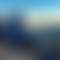 People sitting on a mountain ledge at sunset, wearing winter clothing. Blue sky, distant mountains, and a relaxed, contemplative mood.