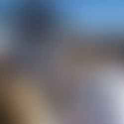 People in religious attire gather outside around a large cross on a sunny day. One person reads from a book, while others observe solemnly.