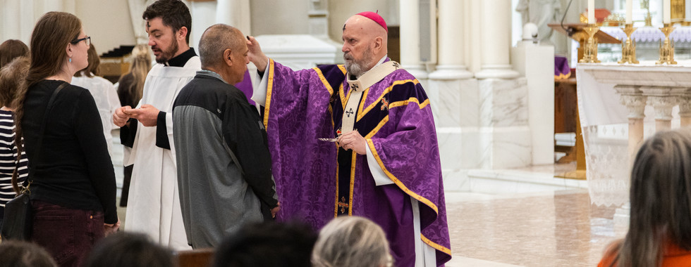Bishop in purple robes marks a man's forehead with ashes. Ornate cathedral and congregation visible in background. Reverent mood.