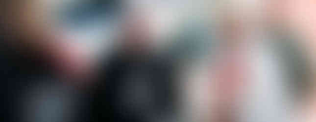 Religious figures in ceremonial robes converse outside near a van with Maltese crosses. Bright lighting, friendly atmosphere.