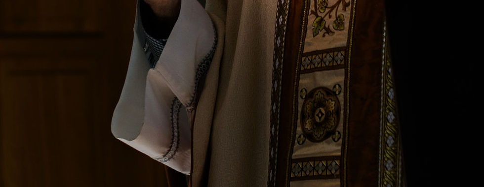 A beam of sunlight shines on a bishop raised hand and vestments during a liturgical celebration, creating a dramatic moment of prayer and blessing.