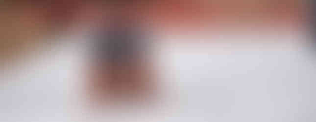 Smiling woman crawling under red ropes on a wet tarp, wearing a blue shirt. The setting appears outdoors with orange cones in the background.