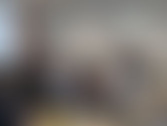 A nun speaks at a podium in a room with attendees seated at tables. Some guests take photos with phones. The mood is attentive.