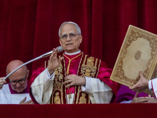 A man in ornate red and gold robes speaks into a microphone on a balcony, holding a gesture. Another holds a large book. Red curtain backdrop.