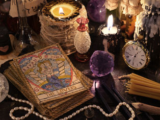 Tarot card "The Lovers" amid candles, clock, and crystals on a mystical table. Warm glow and vintage objects create an enchanting setting.