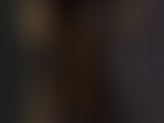 Monk in a hooded brown robe holds a jar, standing barefoot in a dimly lit setting, creating a somber and mysterious mood.